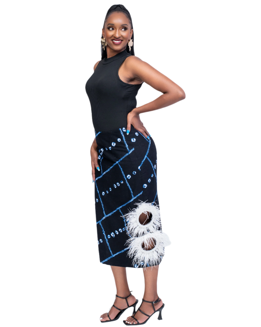 Woman wearing a black sleeveless top and a black and blue patterned skirt with white feather details on a white background